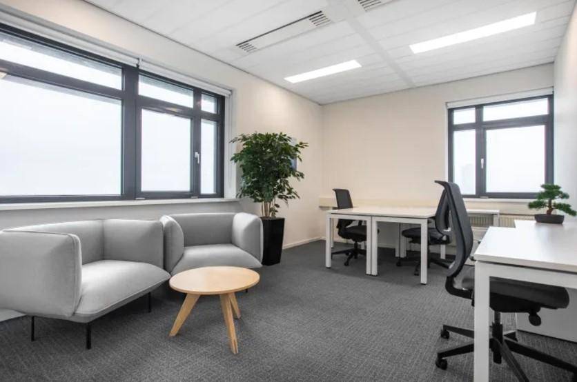 Geräumiges Büro mit mehreren Arbeitsplätzen, Sitzbereich und großen Fenstern.