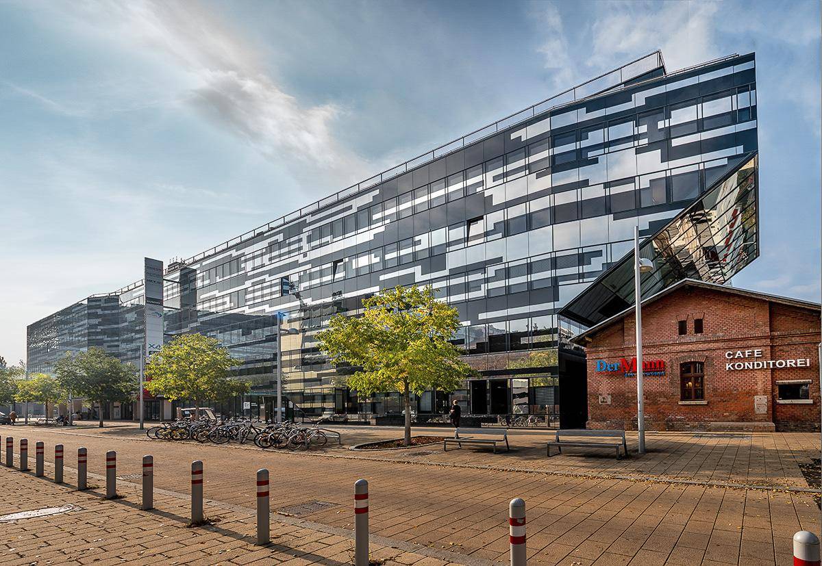 Modernes Bürogebäude mit markanter Glasfassade neben einem historischen Backsteingebäude an einer Straße.