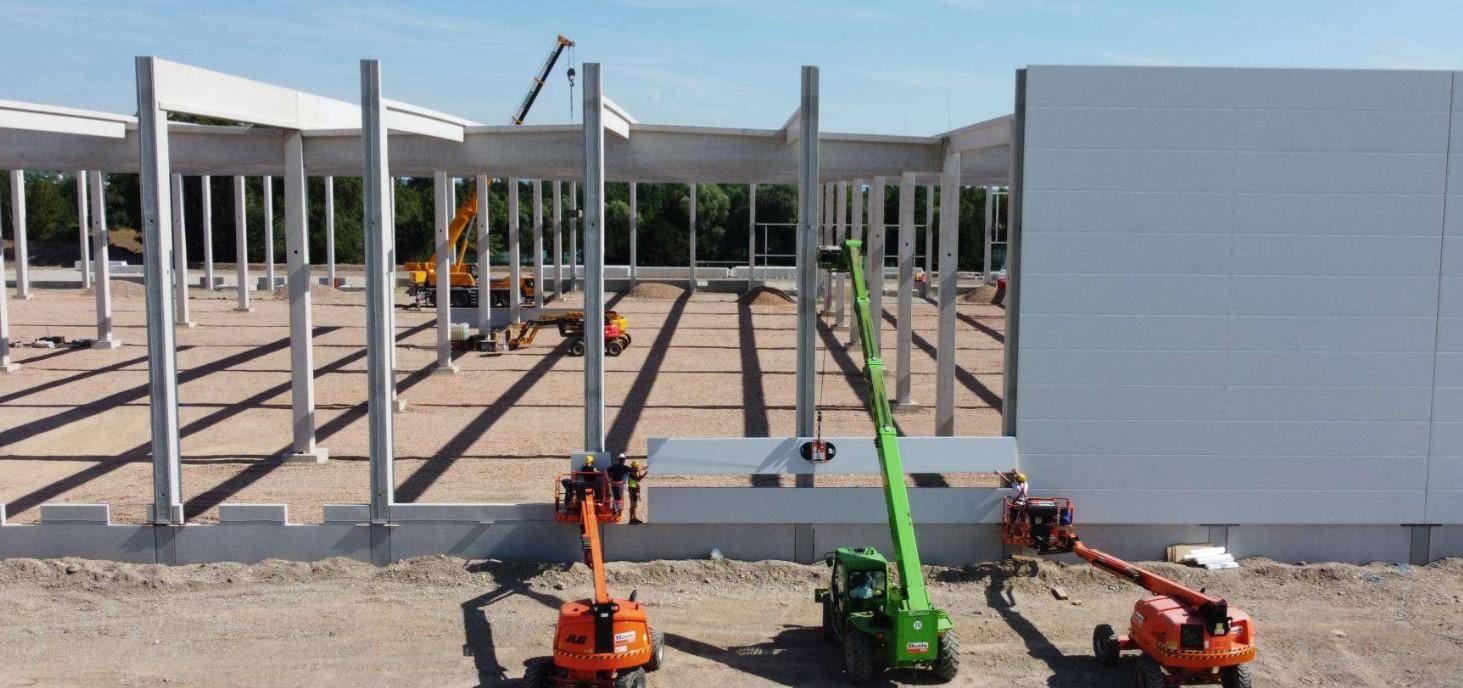 Baustelle einer großen Halle mit sichtbarer Betonrahmenkonstruktion und Montage von Wandelementen.