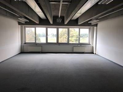 Leerer Büroraum mit großen Fenstern, die viel Tageslicht hereinlassen und einen weiten Blick bieten.