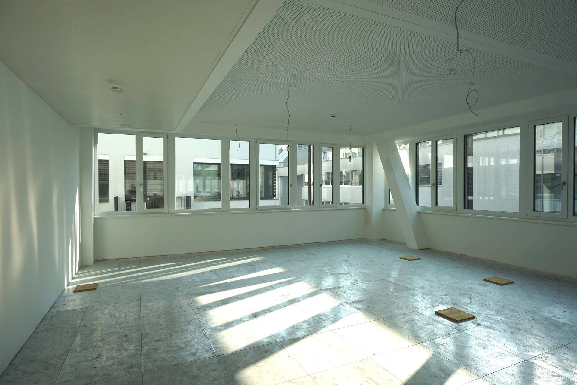 Geräumiger Büroraum mit Fliesenboden, großen Fenstern und viel natürlichem Licht.