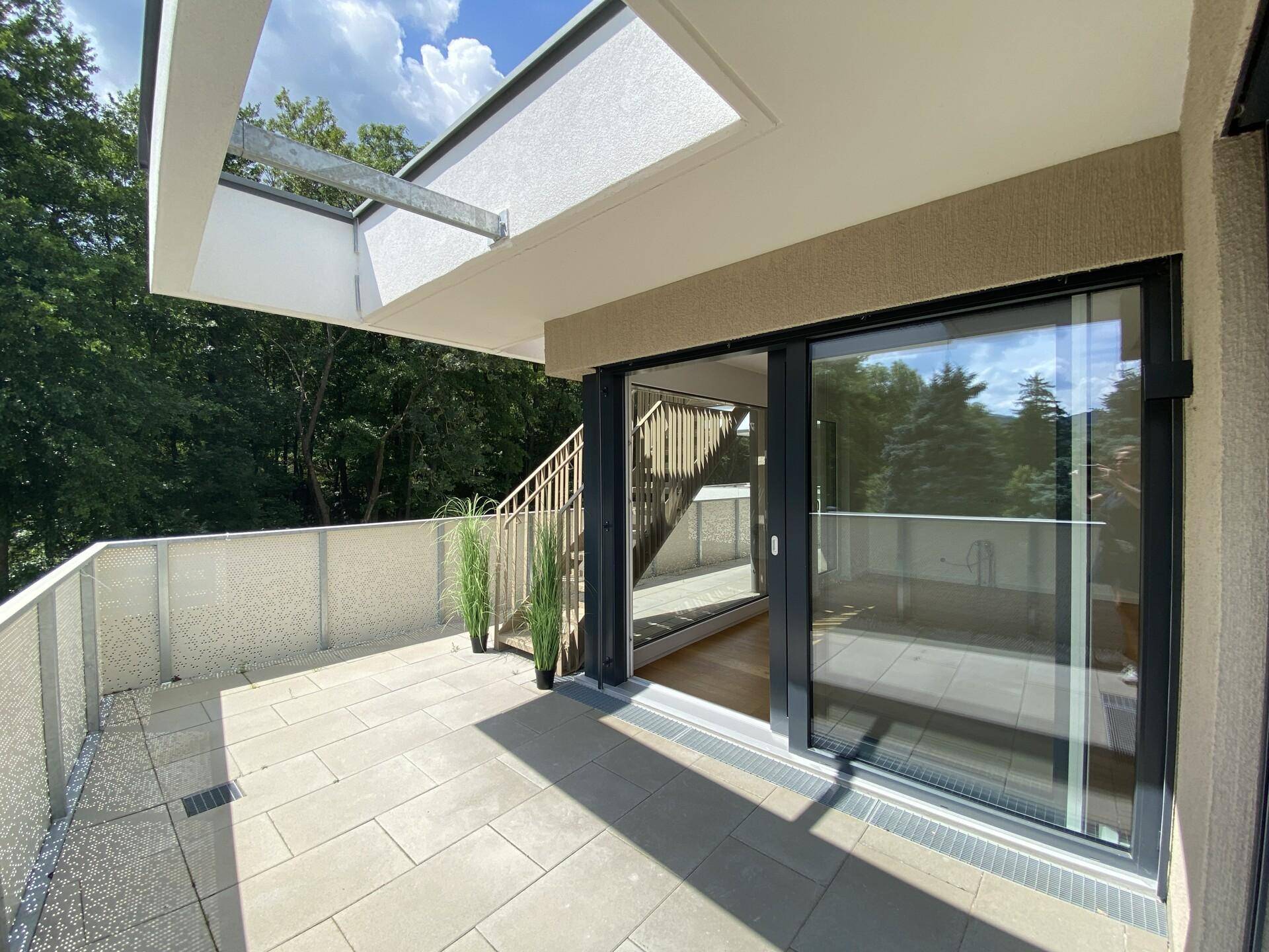 Geräumiger Balkon mit modernen Fliesen, großen Glasschiebetüren und Blick ins Grüne.