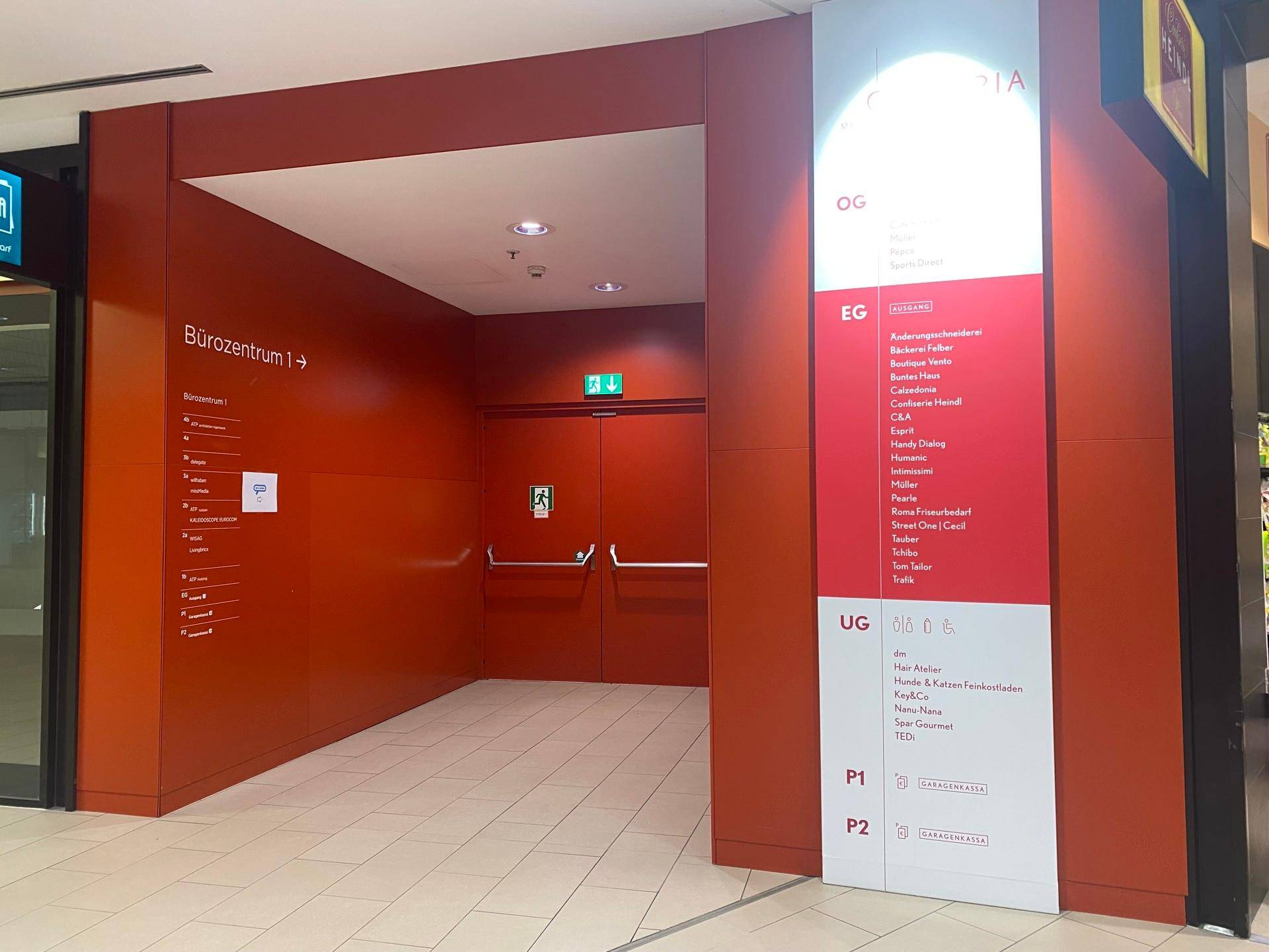 Eingangsbereich eines Bürozentrums mit roter Wandverkleidung und einem großen Verzeichnis der Geschäfte und Büros.