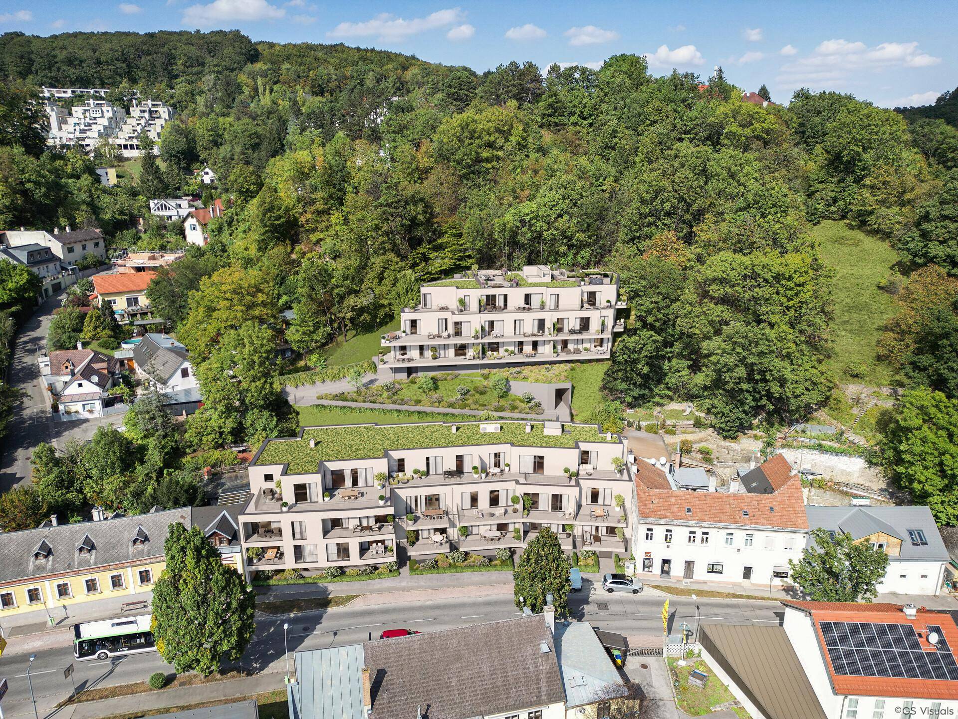 Luftaufnahme von modernen Wohngebäuden mit begrünten Dächern, eingebettet in eine hügelige Waldlandschaft.