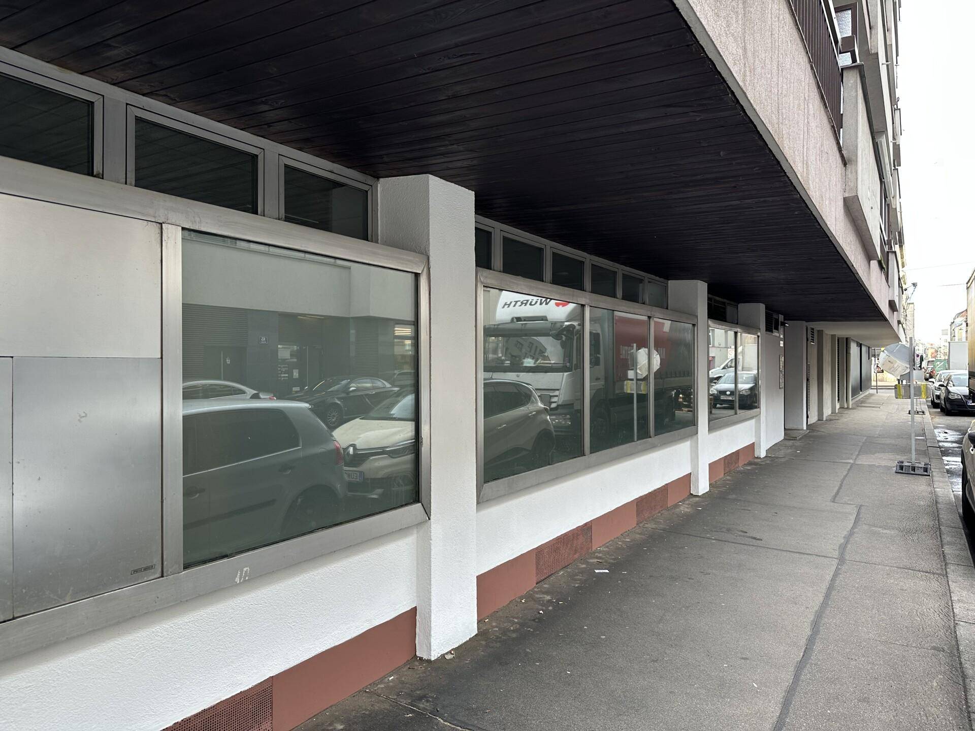 Überdachter Gehweg entlang der Geschäftsfronten eines Gebäudes mit reflektierenden Fenstern und einer langen Perspektive.