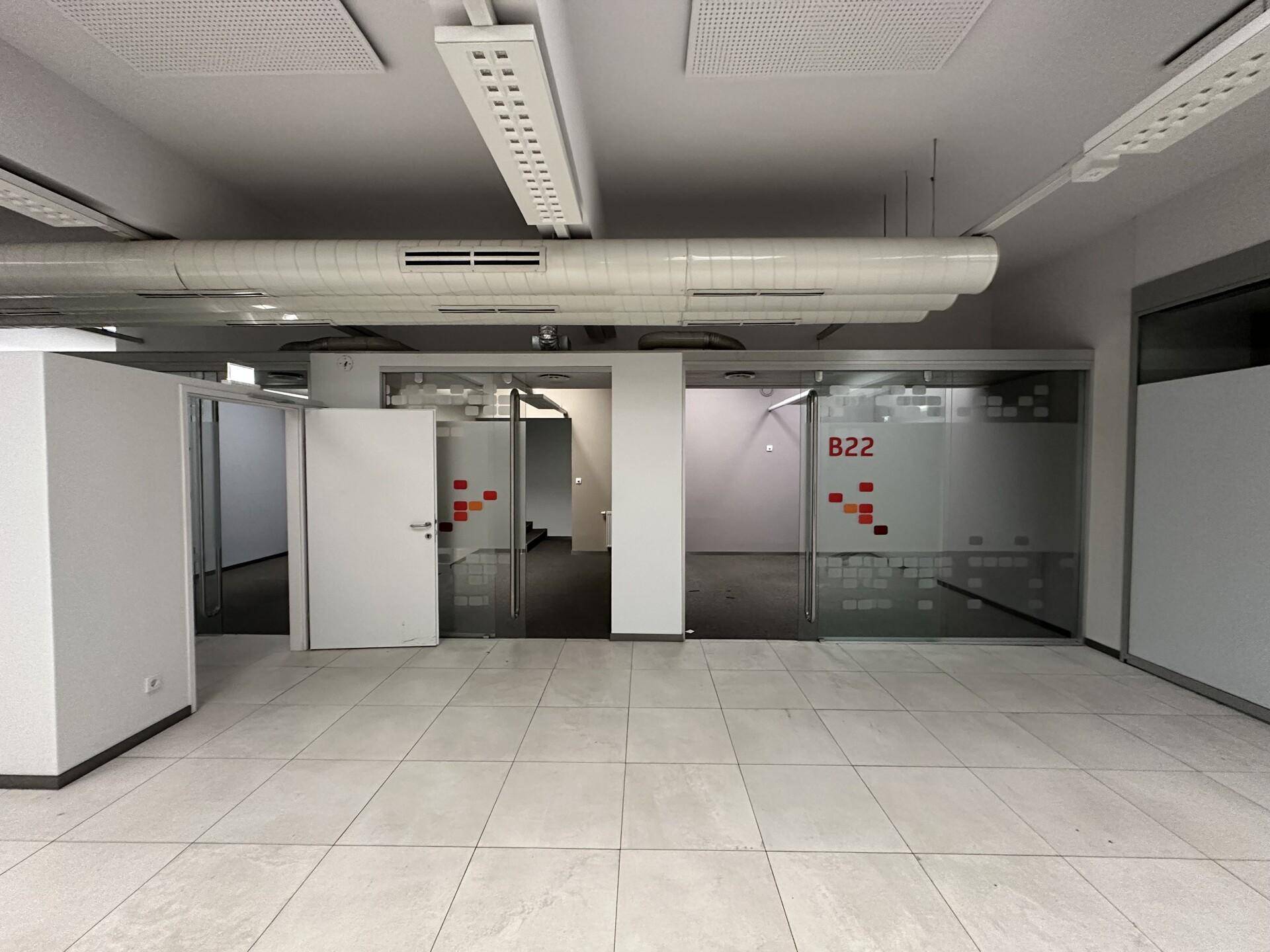 Offener Bürobereich mit Fliesenboden, Glastüren und -wänden, die separate Arbeitsbereiche abgrenzen und viel Licht bieten.