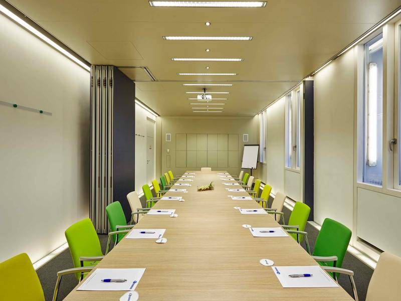 Langer Konferenzraum mit modernem Tisch, vielen Stühlen und einem Projektor an der Decke für Präsentationen.