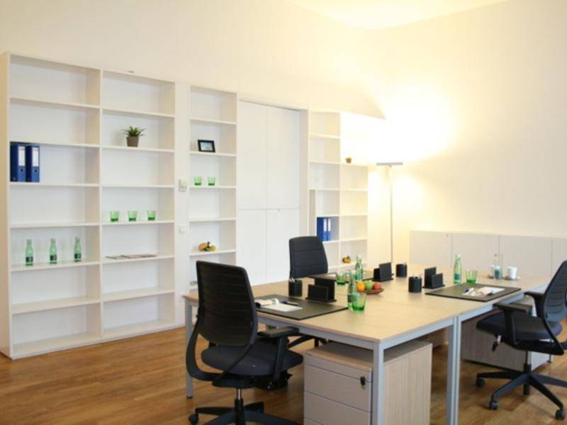 Großes Büro mit mehreren Arbeitsplätzen, weißen Regalen und einem warmen Holzboden.