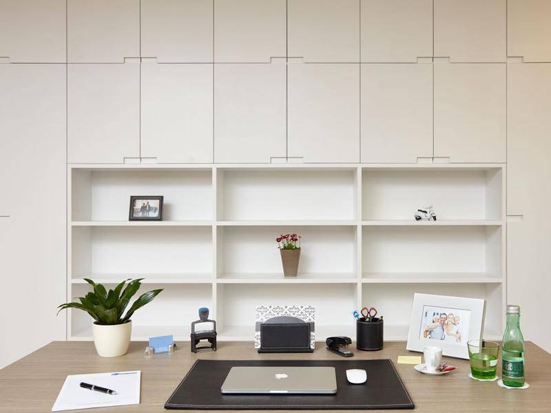 Detailansicht eines aufgeräumten Schreibtisches in einem Büro mit weißen Regalen und dekorativen Pflanzen.