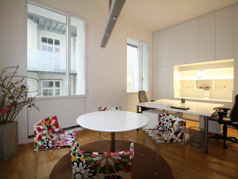 Modernes Büro mit weißem Schreibtisch, bunten Stühlen und praktischen, eingebauten Schränken für Stauraum.