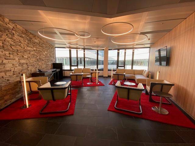 Stilvolle Lounge mit bequemen Sesseln, Sofas, einer Steinwand und großen Fenstern, die viel Licht hereinlassen.