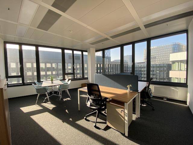 Offenes Büro mit mehreren Arbeitsplätzen, großen Fenstern und viel natürlichem Licht, das den Raum durchflutet.
