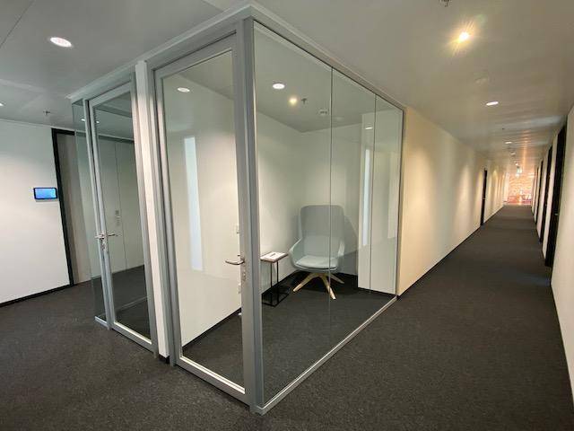 Moderner Bürogang mit Teppichboden und gläsernen Besprechungsboxen, die Privatsphäre bieten.