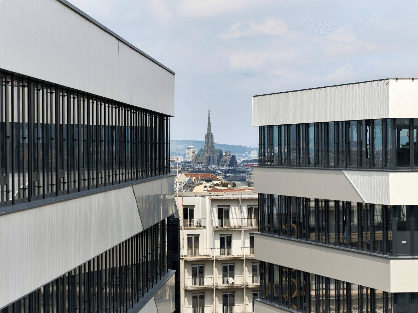Blick aus einem modernen Bürogebäude auf die Stadtlandschaft mit einer historischen Kirchturmspitze in der Ferne.