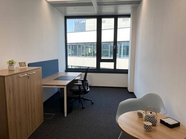Kleines, helles Einzelbüro mit modernem Schreibtisch, Bürostuhl und einem kleinen Beistelltisch am Fenster.