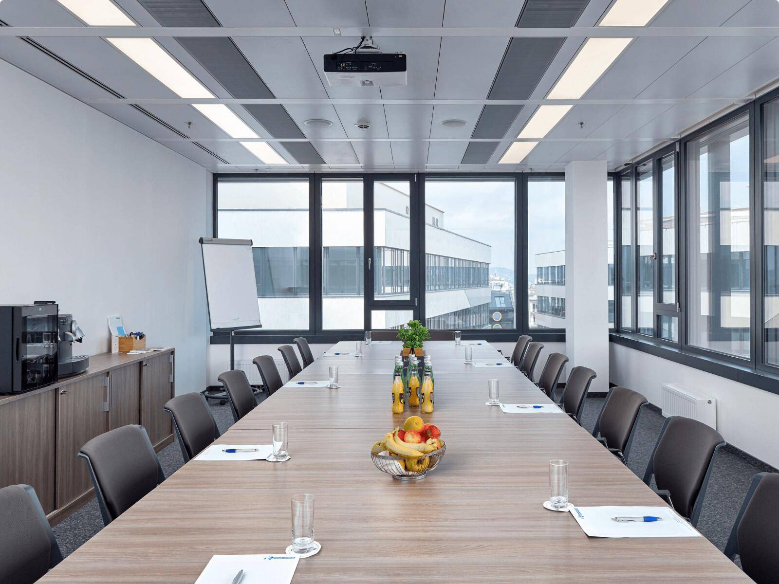 Großer Konferenzraum mit langem Holztisch, vielen Stühlen und großen Fenstern, die viel Tageslicht hereinlassen.