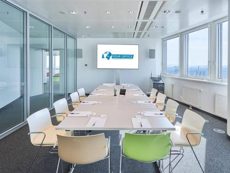 Moderner Konferenzraum mit großem Tisch, bequemen Stühlen und Stadtblick durch große Fenster.
