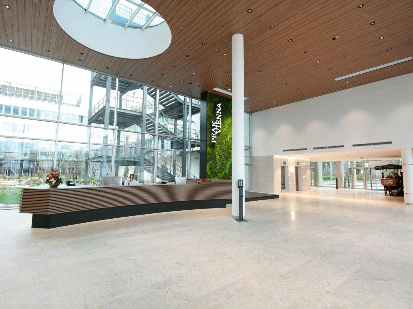 Großzügige, moderne Lobby mit hoher Decke, Empfangsbereich, viel Tageslicht und Blick ins Grüne.