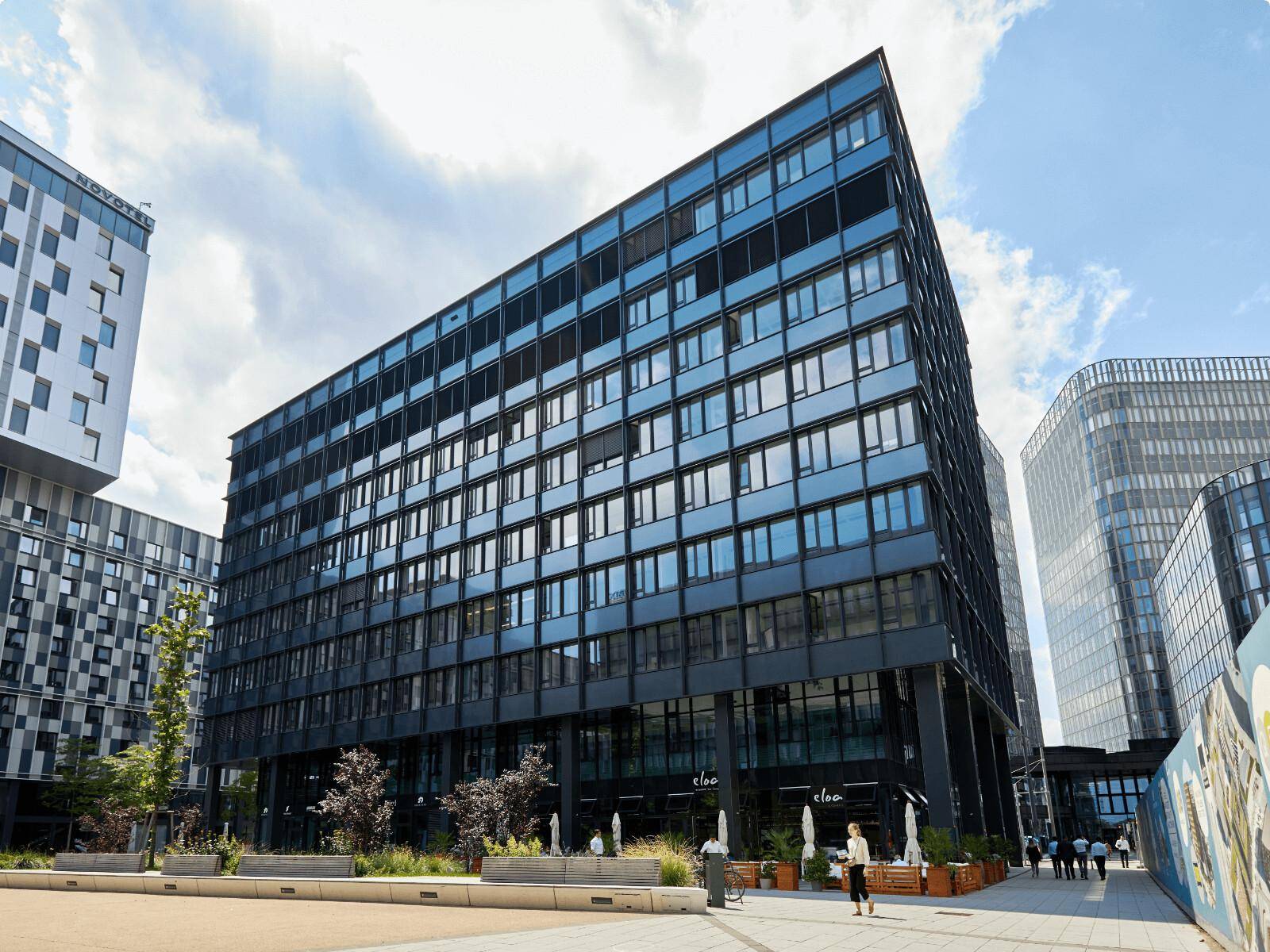 Zeitgenössisches Bürogebäude mit dunkler Glasfassade und Geschäften im Erdgeschoss unter blauem Himmel.