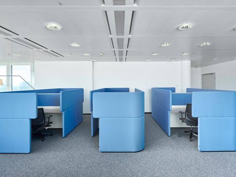 Moderne Bürozellen mit blauen Trennwänden, ergonomischen Stühlen und Teppichboden.