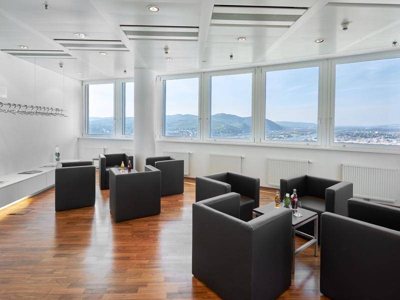 Gemütlicher Lounge-Bereich mit dunklen Sesseln, Holzboden und Panoramablick auf die Landschaft.