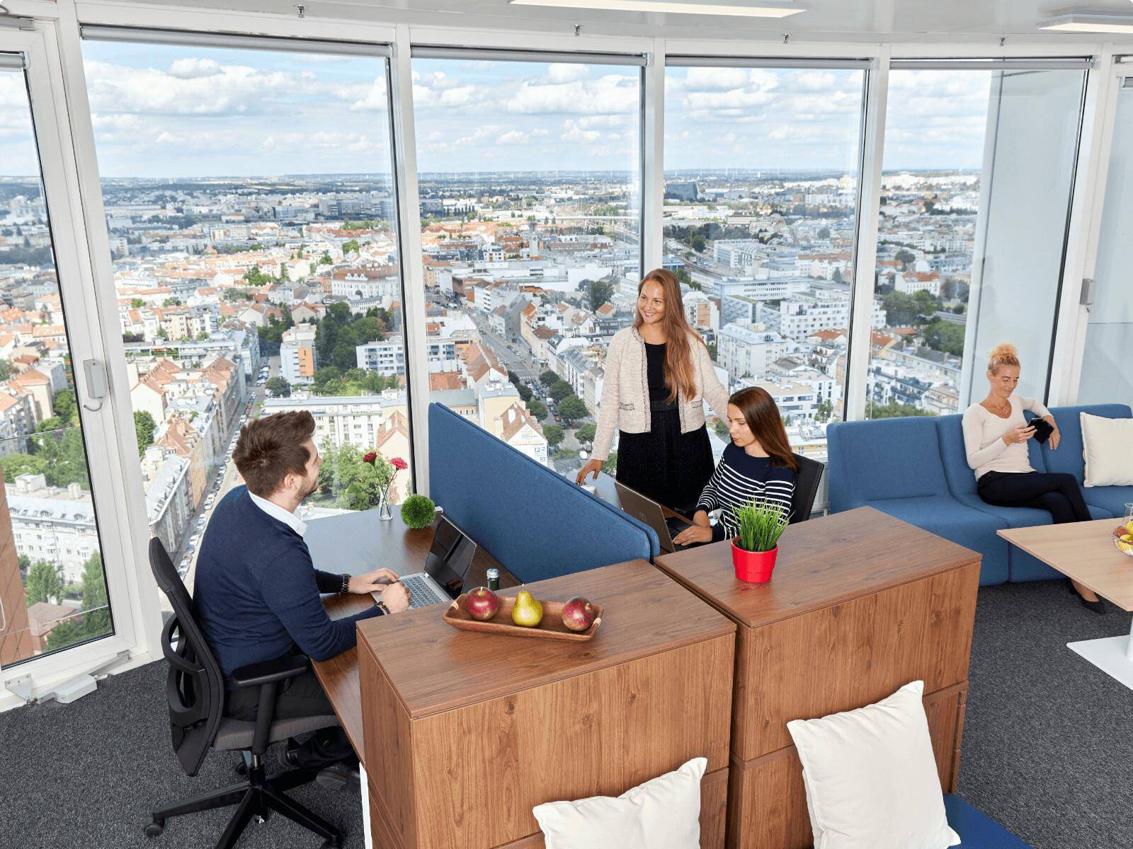 Modernes Großraumbüro mit Arbeitsplätzen, Sitzgelegenheiten und Panoramablick auf die Stadt.