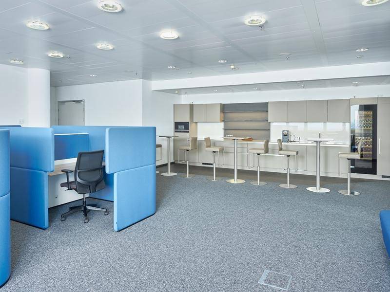 Moderne Büroküche mit grauen Schränken, Bartischen und Teppichboden.