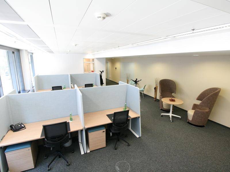 Offener Bürobereich mit Arbeitsplätzen, Trennwänden und einer kleinen Lounge-Ecke.
