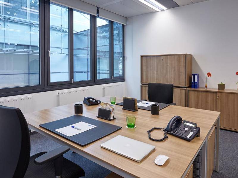 Einzelbüro mit Holztisch, Bürostühlen und großen Fenstern mit Blick nach draußen.