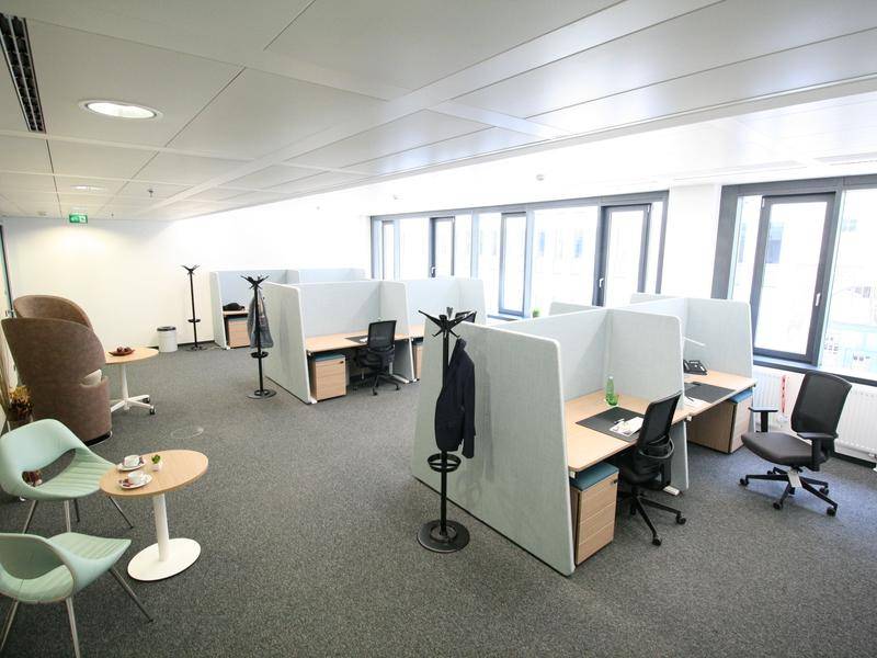 Geräumiger Bürobereich mit mehreren Arbeitsplätzen, Sitzgelegenheiten und großen Fenstern.