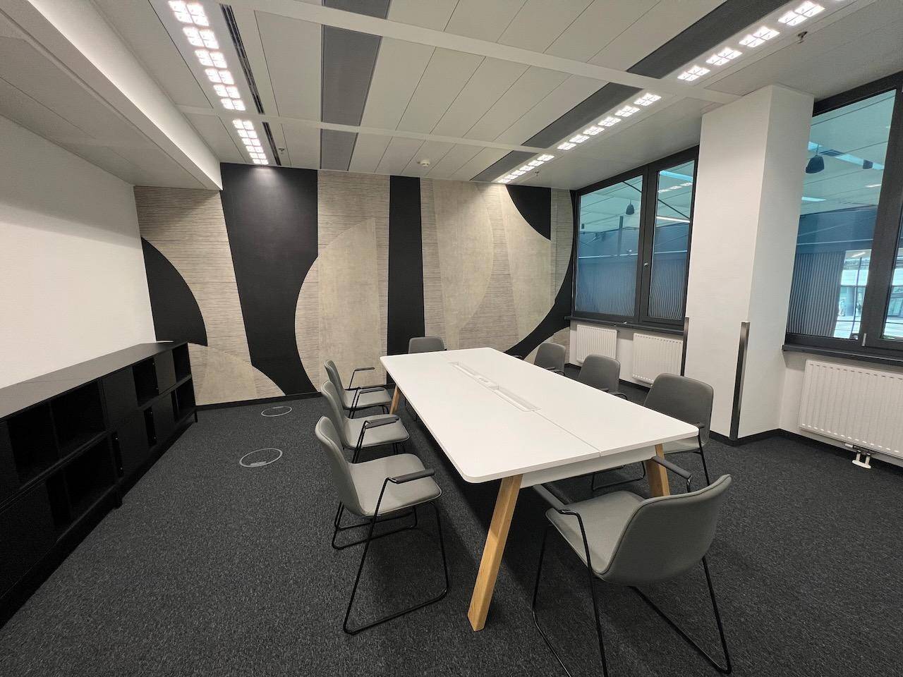 Modern eingerichteter Besprechungsraum mit abstraktem Wanddesign und Blick nach draußen.