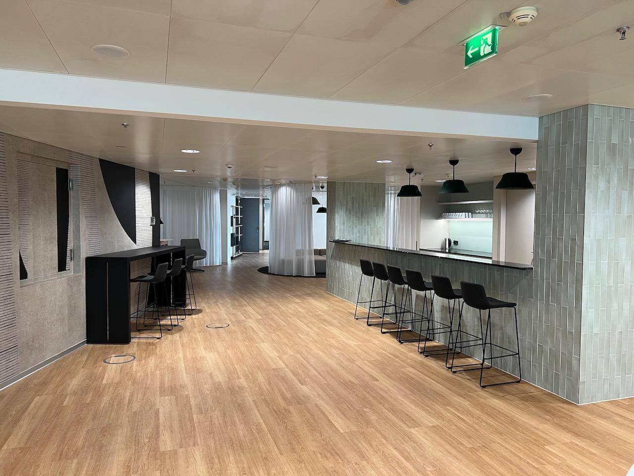 Moderne Bar mit hohen Hockern, Holzboden und stilvollen Hängelampen.