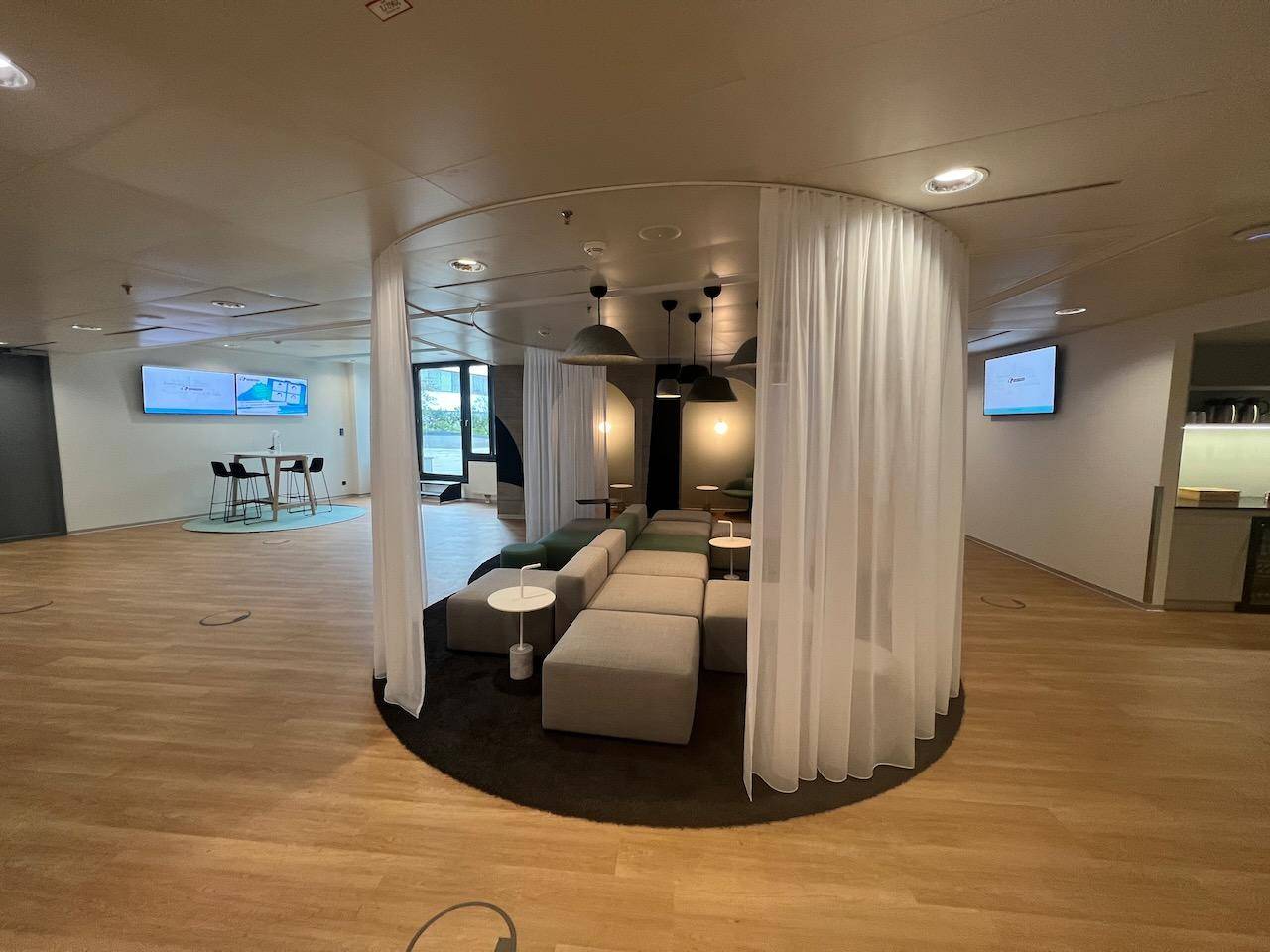 Weitläufiger Lounge-Bereich mit zentraler Sitzgruppe, Vorhängen und Holzboden.