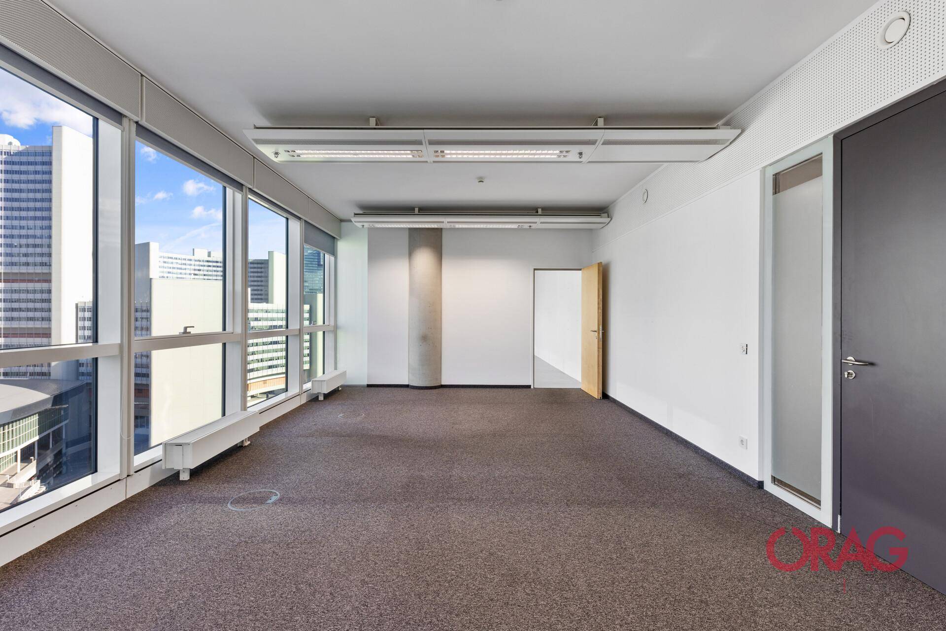 Helles Büro mit Teppichboden, großen Fenstern und Zugang zu weiteren Räumen in einem modernen Gebäude.