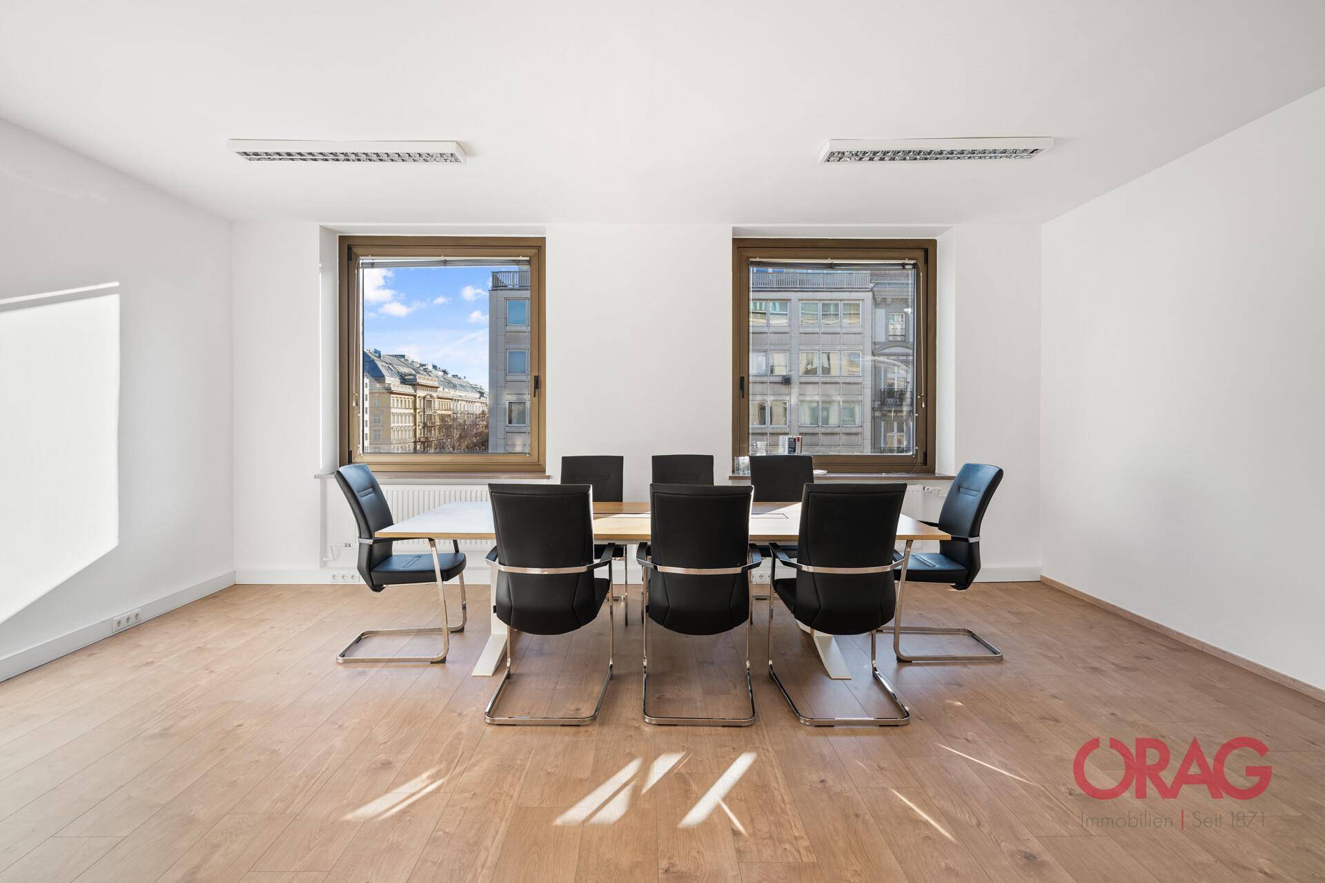 Helles Büro mit Holzboden, großem Konferenztisch und Fenstern mit Blick auf die umliegende Stadt.