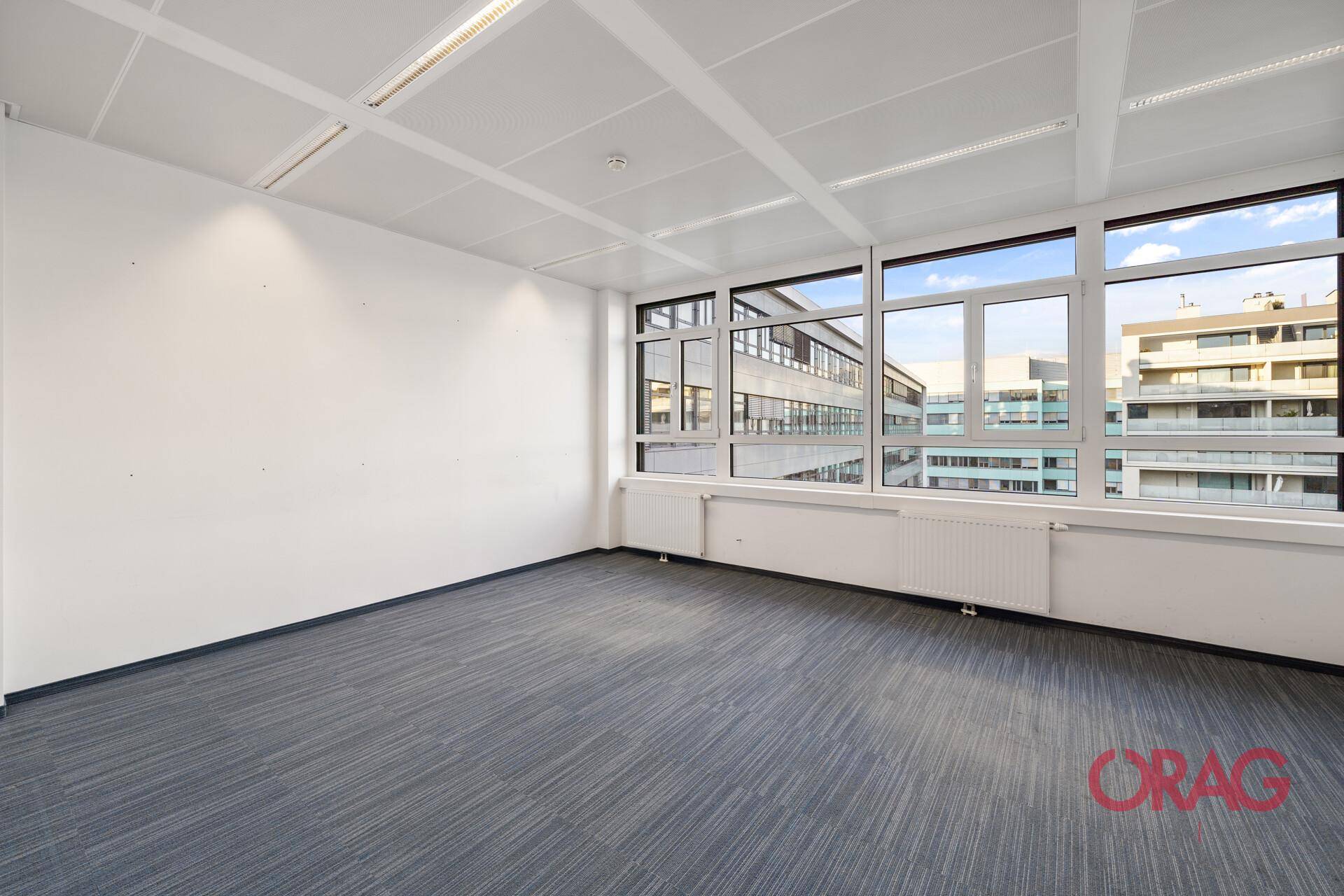 Leeres Büro mit großen Fenstern, die einen weiten Blick auf die Stadt und viel natürliches Licht bieten.