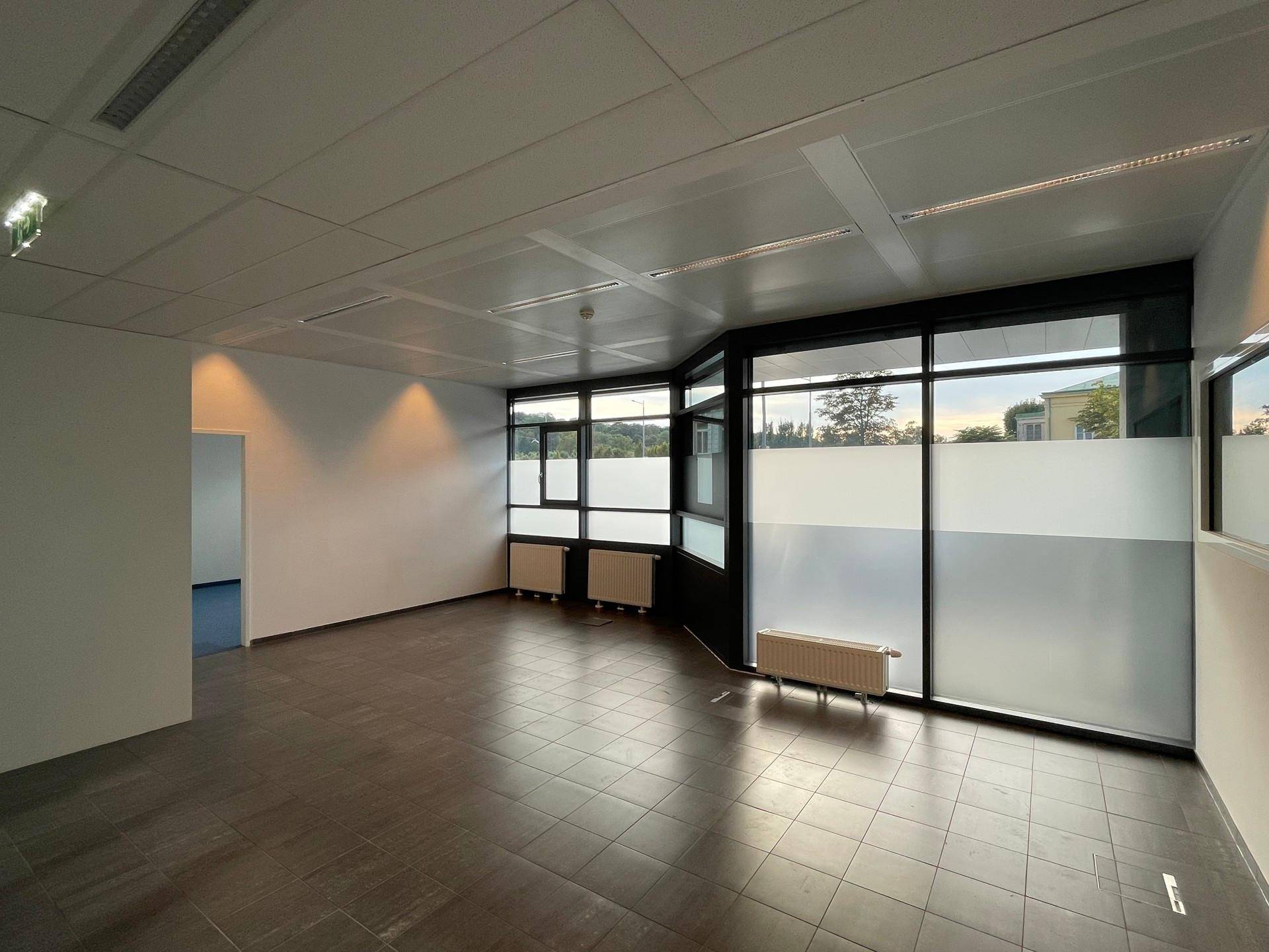Helles Büro mit dunklem Fliesenboden und großen Fenstern, die einen Blick ins Grüne ermöglichen.