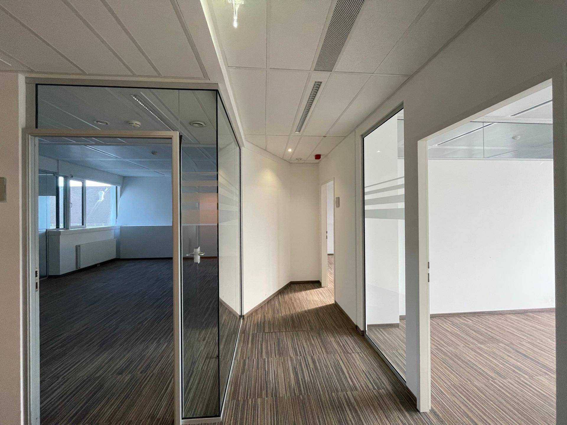 Moderner Bürogang mit Teppichboden und Glaswänden, die zu den einzelnen Büros führen.