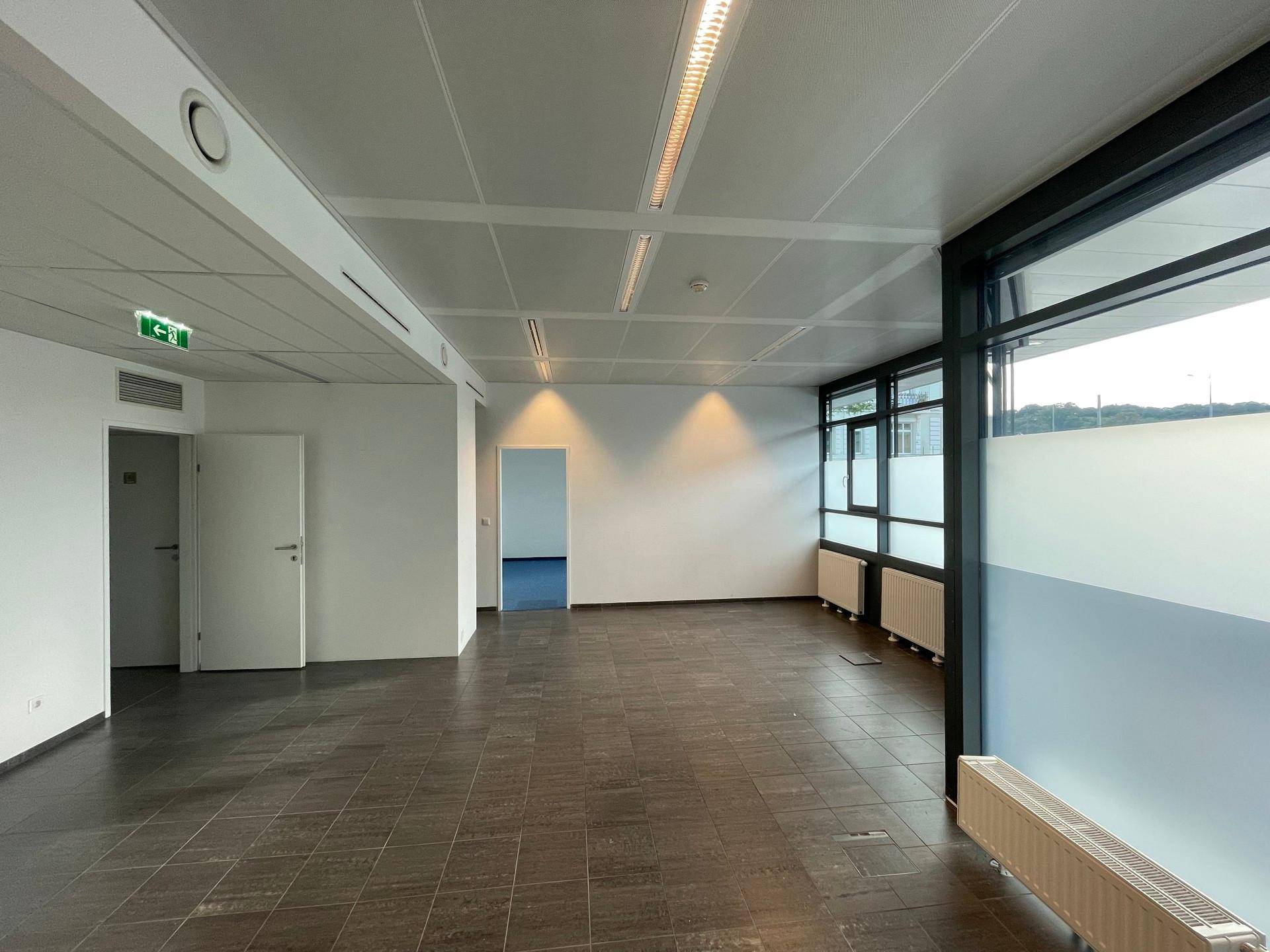 Leeres Büro mit dunklem Fliesenboden und großen Fenstern, teilweise mit Sichtschutzfolie versehen.