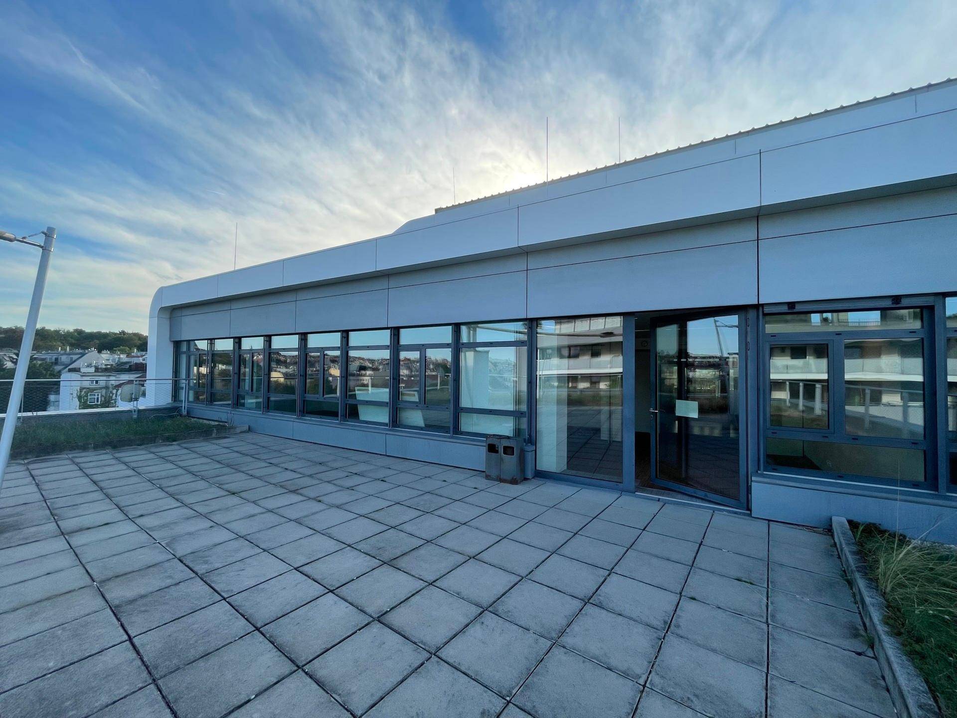 Weitläufige Terrasse mit Zugang zu den Büroräumen durch große Fenster und Glastüren.