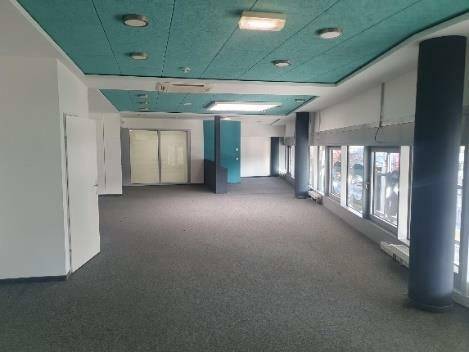 Heller Büroraum mit Teppichboden, Säulen und einer auffälligen grünen Decke.