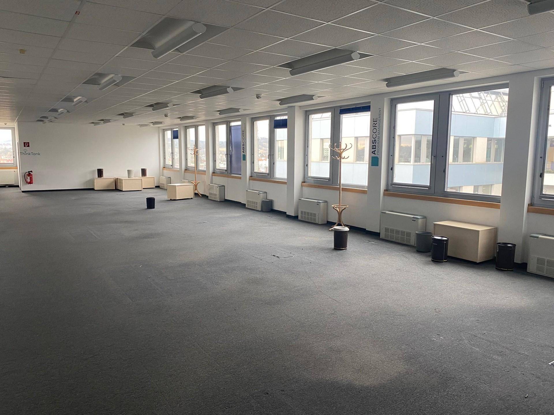 Weitläufiges Großraumbüro mit grauem Teppichboden und durchgehender Fensterfront, ideal für flexible Arbeitsbereiche.