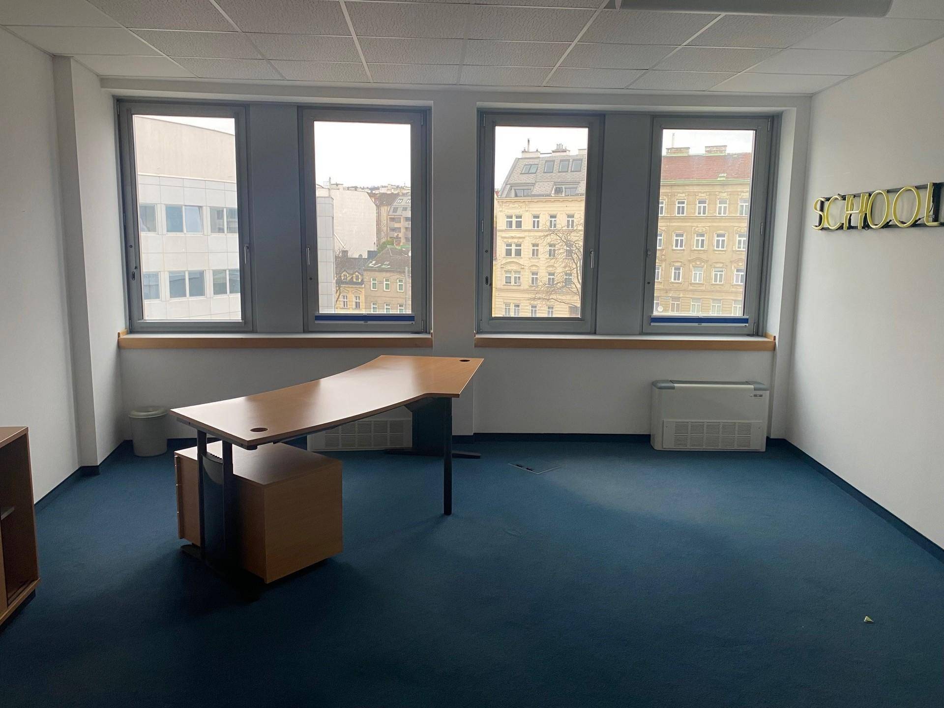 Büro mit blauem Teppichboden, einem einzelnen Schreibtisch und einem "SCHOOL"-Schriftzug an der Wand.