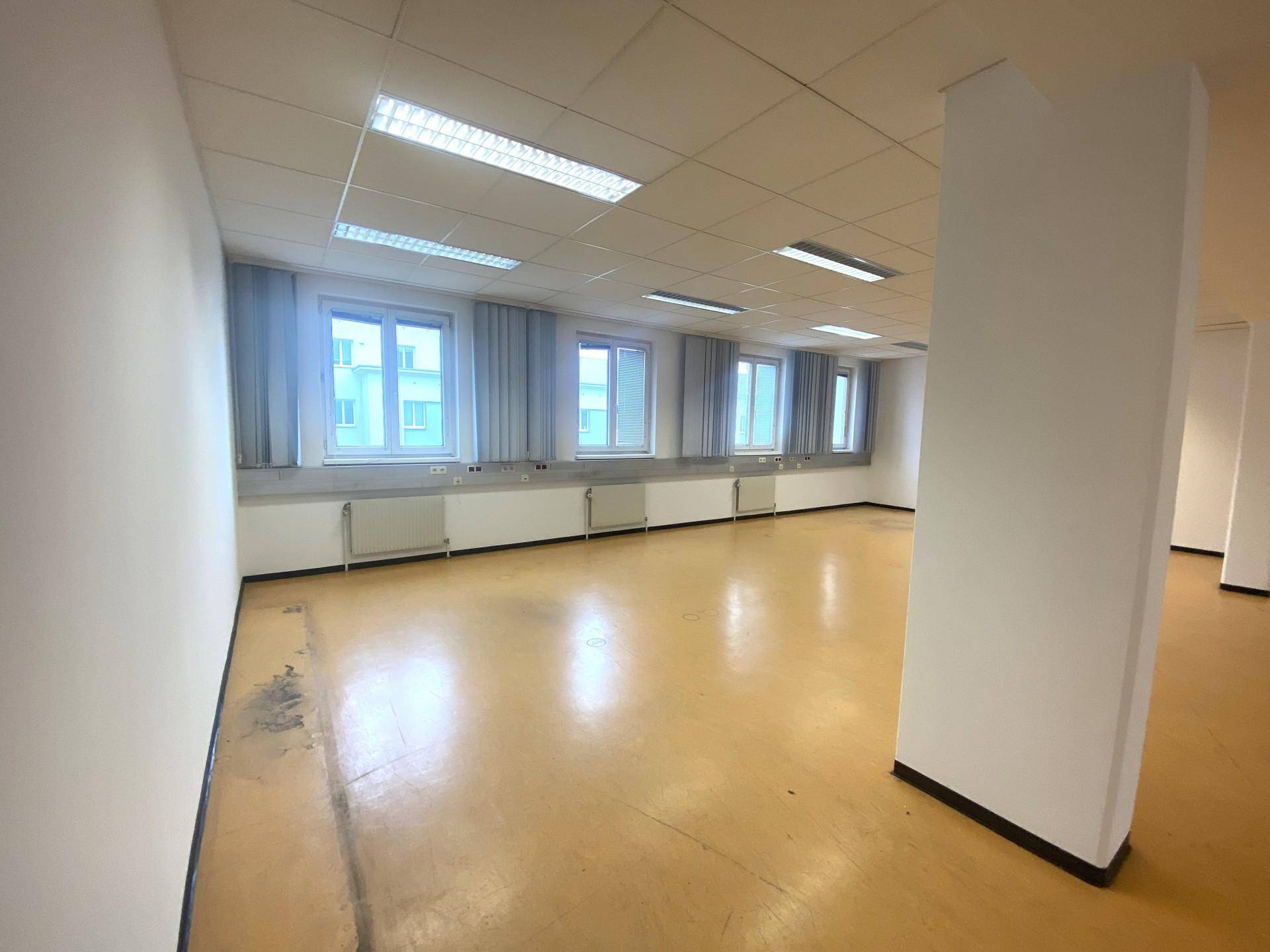 Großer, leerer Büroraum mit gelbem Bodenbelag, vielen Fenstern und Deckenleuchten.