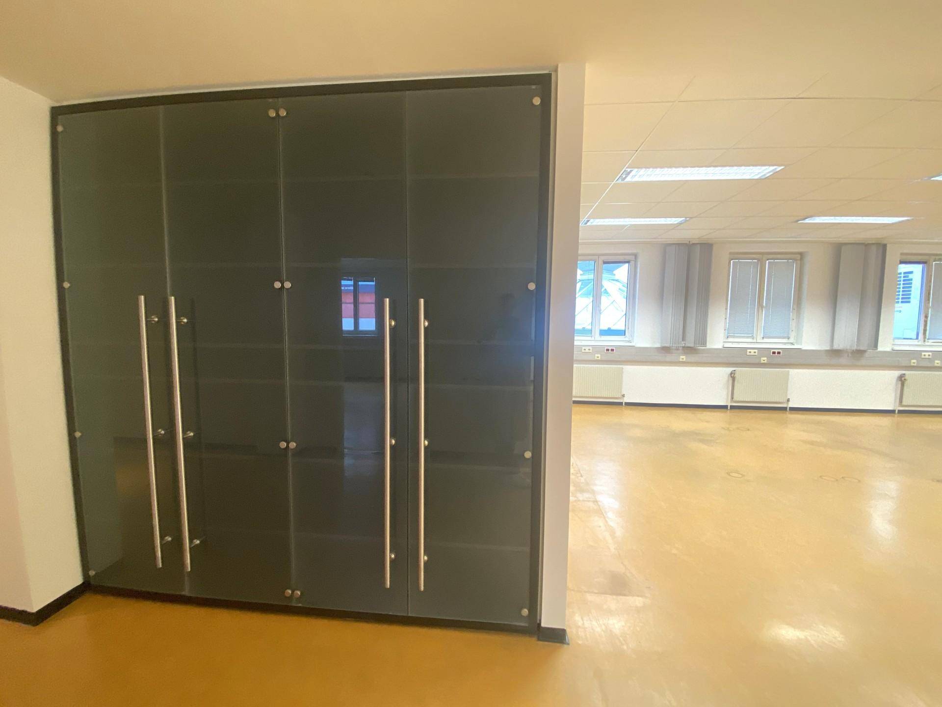 Innenbereich mit modernen Glastüren und Metallgriffen, die zu einem größeren Raum mit gelbem Boden führen.