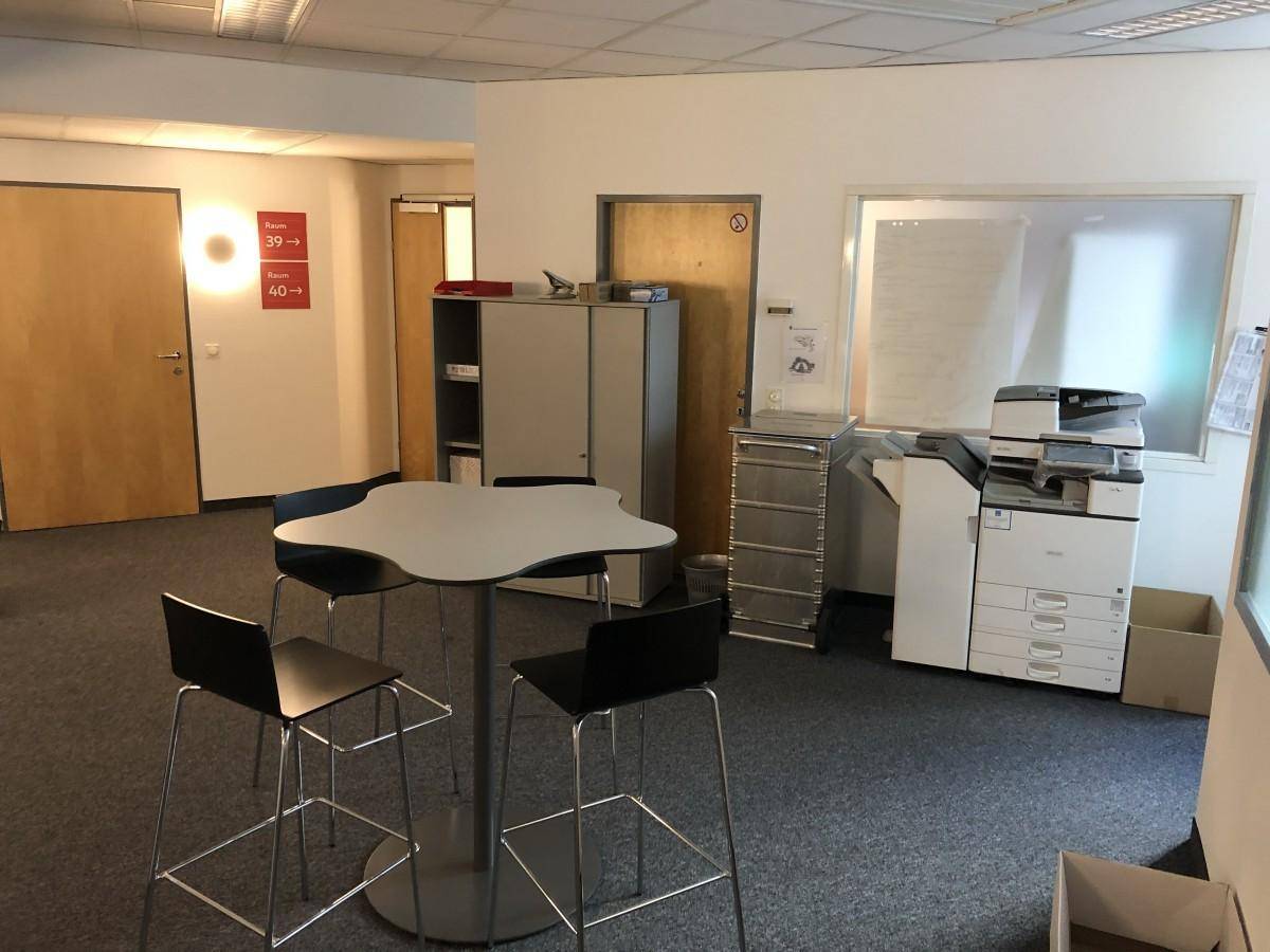 Informeller Bürobereich mit Stehtisch, Barhockern und Kopiergerät in einem modernen Bürogebäude.