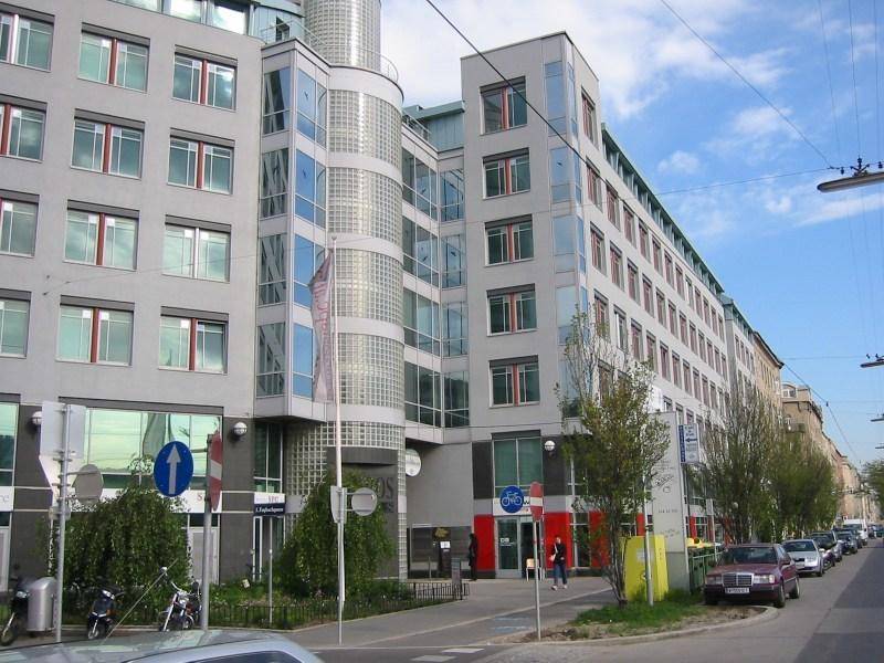 Großes modernes Bürogebäude mit markantem Glasturm und vielen Fenstern an einer belebten Straße.
