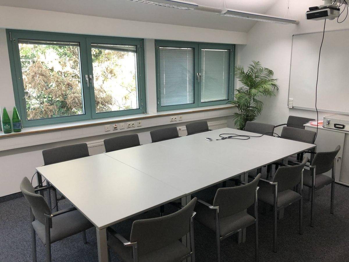 Funktionaler Konferenzraum mit großem Besprechungstisch, bequemen Stühlen und Fenstern mit Blick ins Grüne.