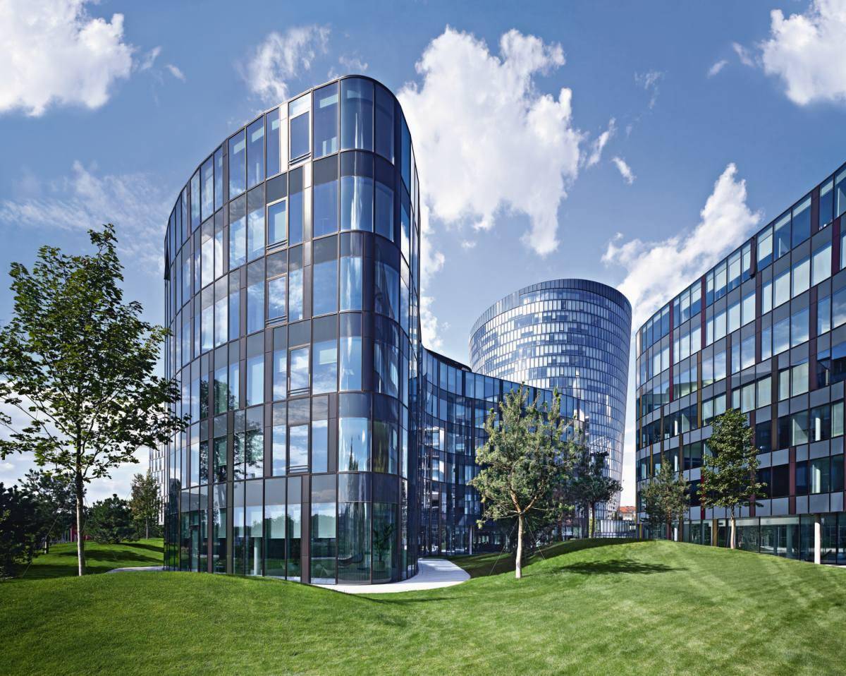 Moderne Bürogebäude mit geschwungenen Glasfassaden umgeben von grünen Hügeln unter blauem Himmel.