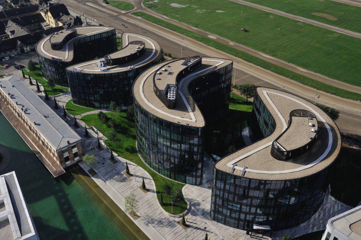 Luftaufnahme eines modernen Bürokomplexes mit geschwungenen Gebäuden und weitläufigen Grünflächen.